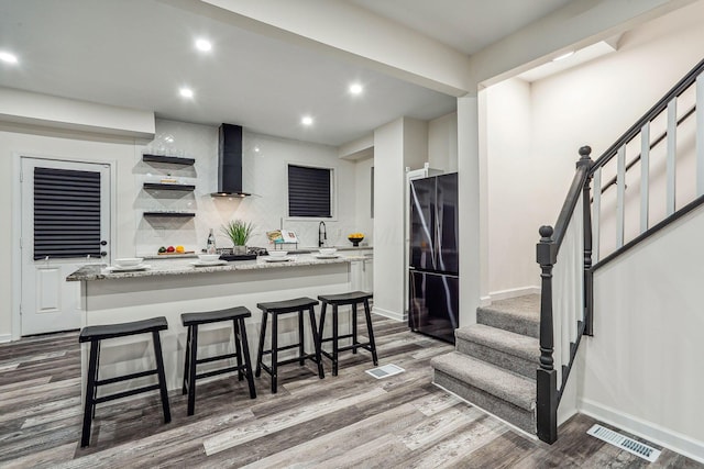 kitchen with black fridge, white cabinetry, wall chimney range hood, and a kitchen island