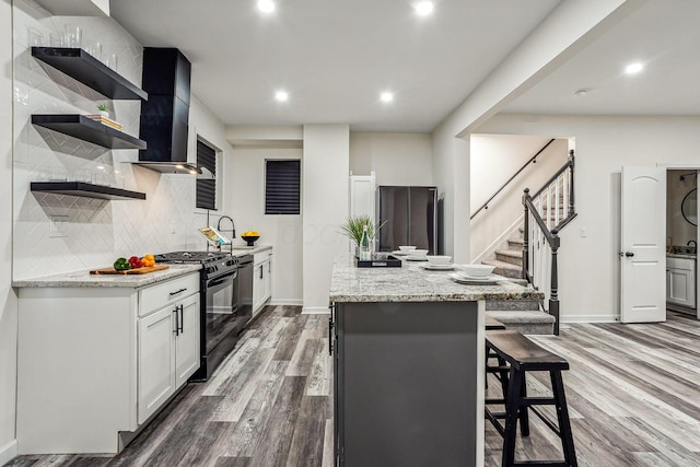 kitchen with black gas range oven, wood-type flooring, a kitchen island, white cabinets, and light stone countertops