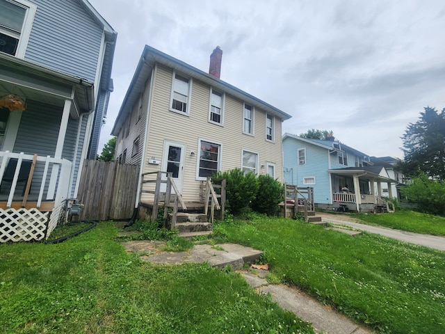 rear view of property featuring a chimney, fence, and a lawn