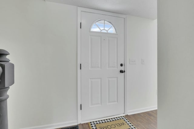 foyer featuring baseboards, wood finished floors, and a textured ceiling