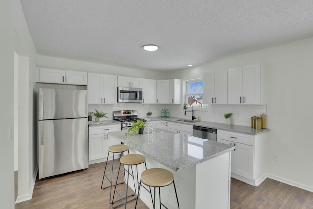 kitchen with appliances with stainless steel finishes, light stone countertops, white cabinets, a sink, and a kitchen island