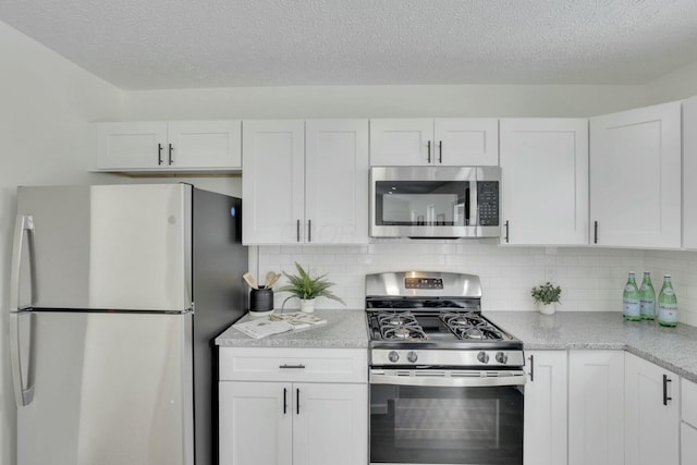 kitchen with a textured ceiling, backsplash, white cabinets, and appliances with stainless steel finishes