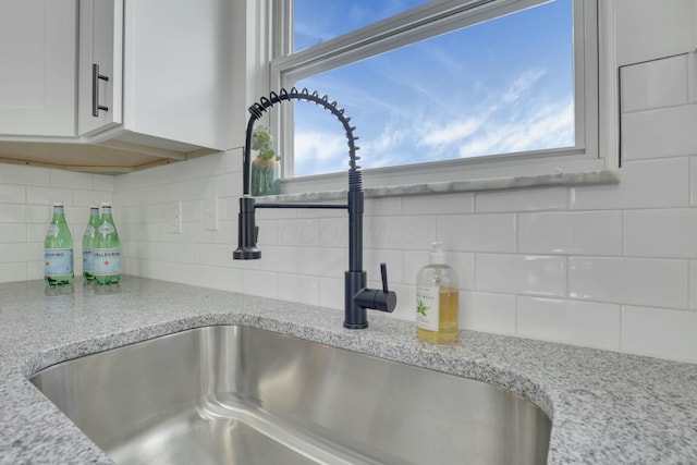 details with white cabinetry, backsplash, light stone countertops, and a sink