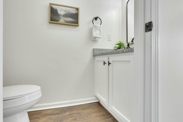 half bathroom featuring vanity, baseboards, wood finished floors, and toilet