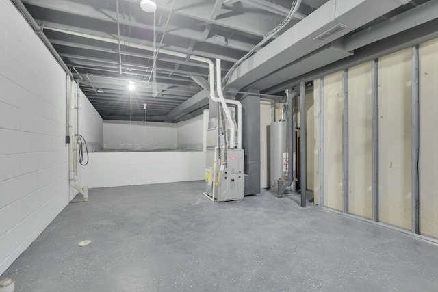 unfinished below grade area featuring visible vents, concrete block wall, heating unit, and water heater