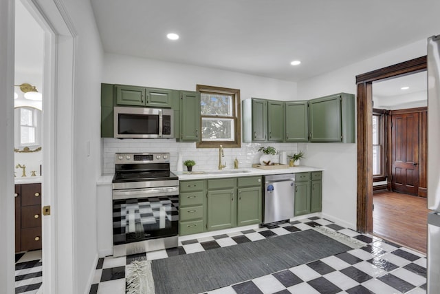 kitchen with light floors, light countertops, appliances with stainless steel finishes, a sink, and green cabinetry