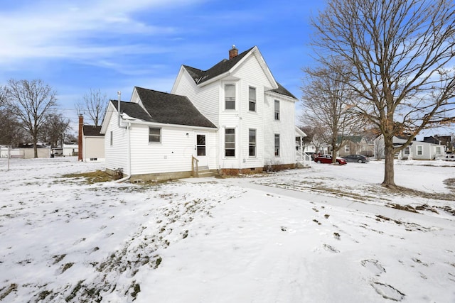 snow covered house featuring entry steps and a chimney