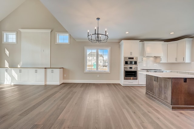 kitchen featuring a chandelier, light wood-style flooring, light countertops, wall chimney range hood, and white cabinetry