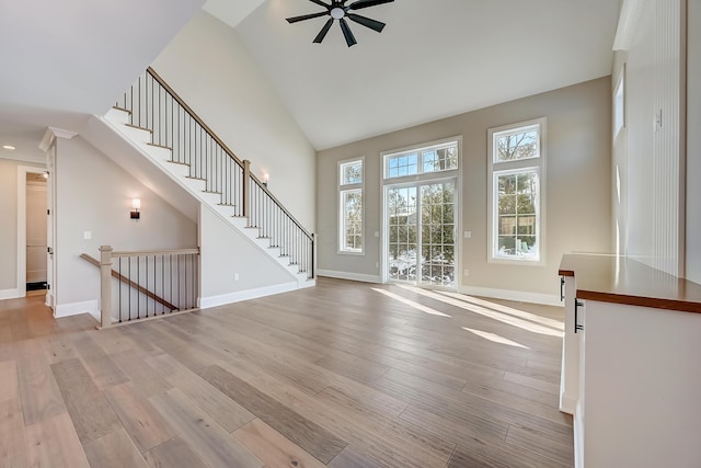 unfurnished living room with baseboards, high vaulted ceiling, ceiling fan, and light wood-style floors