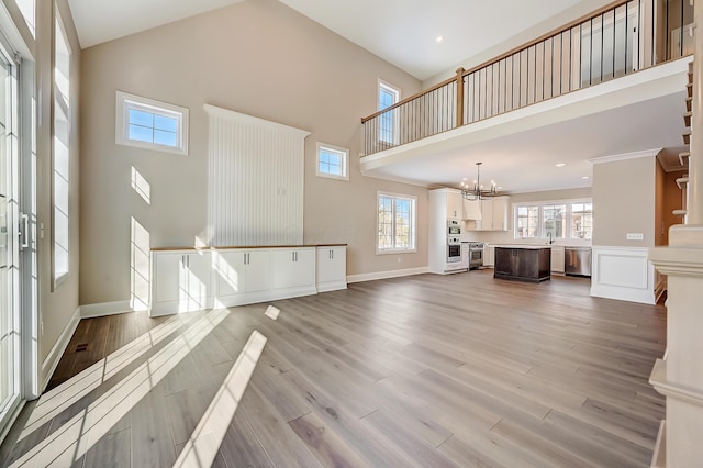 unfurnished living room with a high ceiling, a sink, baseboards, light wood-type flooring, and an inviting chandelier