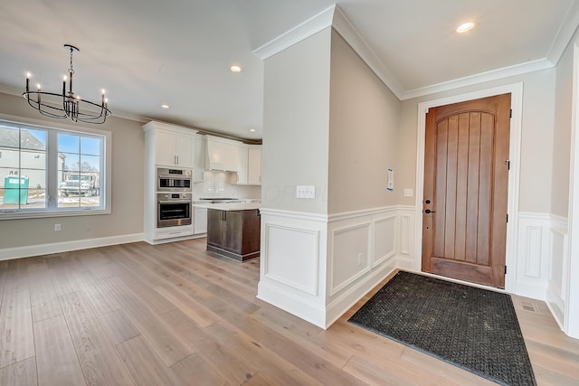 foyer entrance with a chandelier, light wood-style flooring, recessed lighting, wainscoting, and crown molding