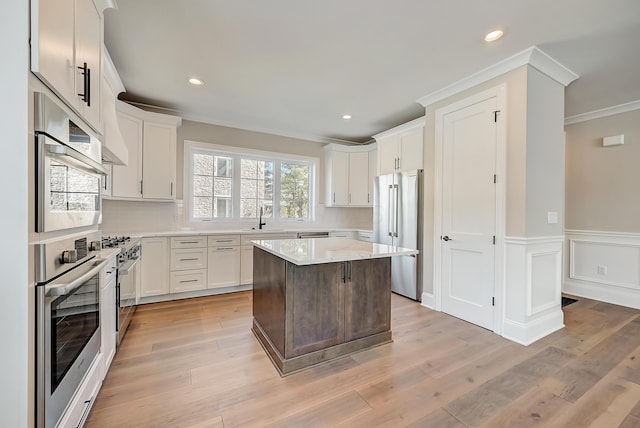 kitchen featuring premium appliances, a center island, crown molding, white cabinetry, and a sink