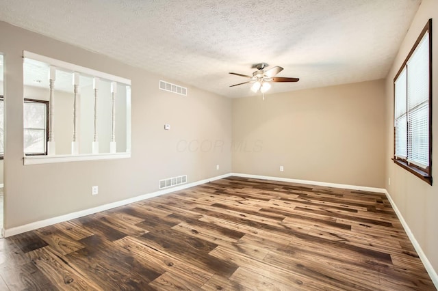 spare room with a textured ceiling, wood finished floors, visible vents, and baseboards