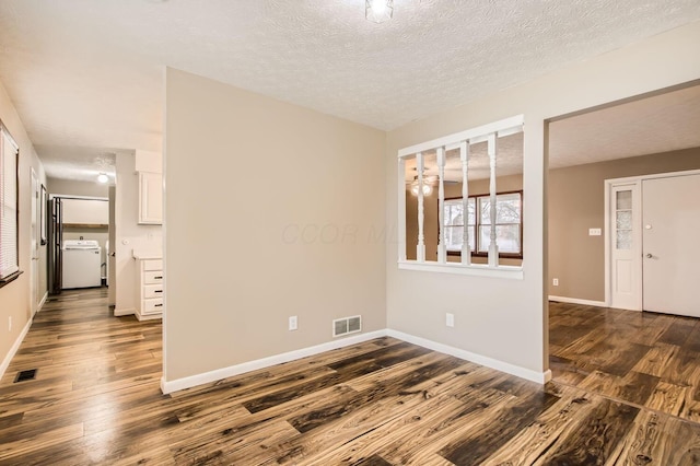 empty room featuring dark wood-style floors, washer / clothes dryer, visible vents, and baseboards