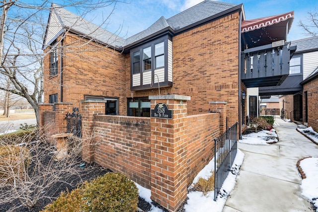 view of snowy exterior with brick siding and fence