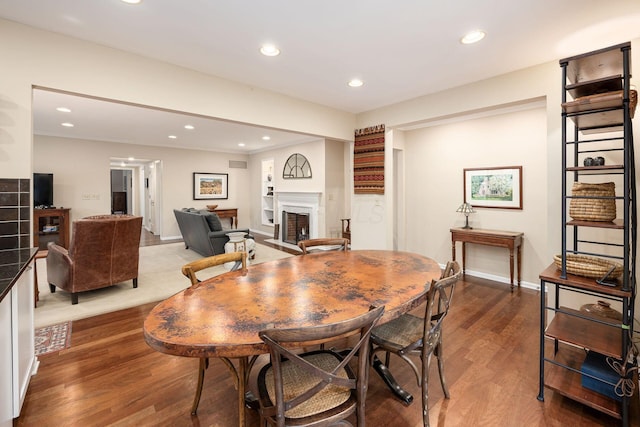 dining room featuring a fireplace, baseboards, wood finished floors, and recessed lighting