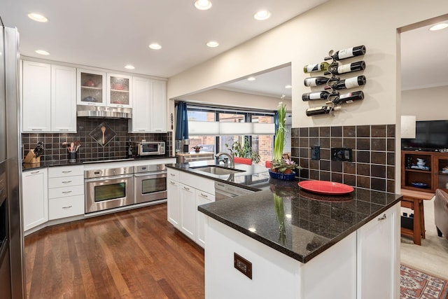 kitchen with dark wood finished floors, glass insert cabinets, white cabinetry, stainless steel oven, and a sink