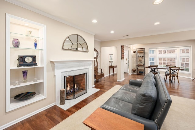 living area with a fireplace with flush hearth, built in shelves, dark wood finished floors, and crown molding