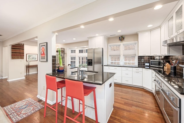 kitchen featuring stainless steel appliances, wood finished floors, a sink, white cabinetry, and a kitchen breakfast bar