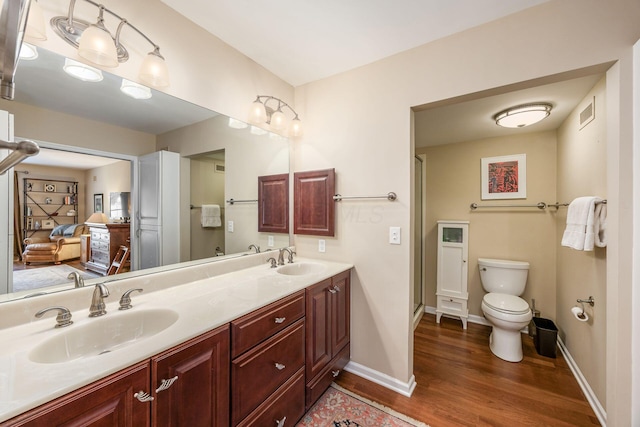 bathroom featuring wood finished floors, a sink, toilet, and double vanity