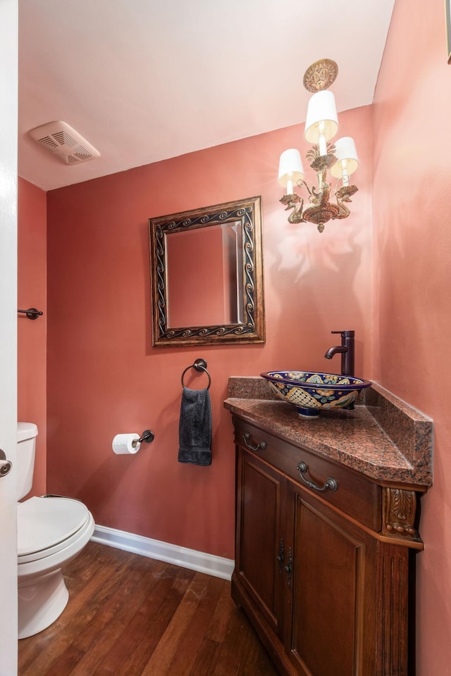 half bathroom with baseboards, visible vents, wood finished floors, vanity, and a notable chandelier