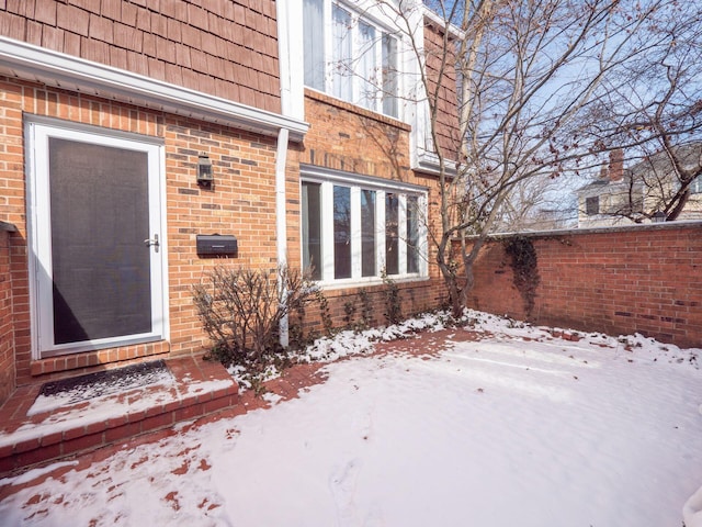 snow covered property entrance featuring brick siding