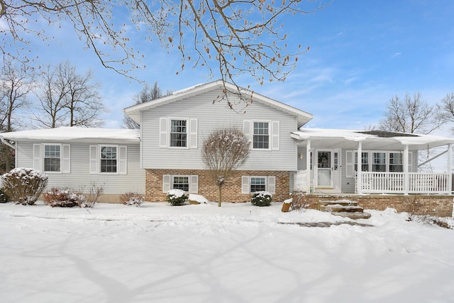 snow covered house featuring a porch and brick siding