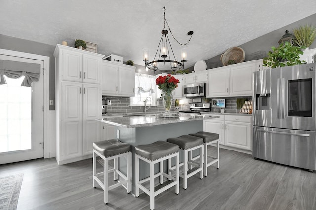 kitchen featuring stainless steel appliances, a center island, white cabinetry, and hanging light fixtures