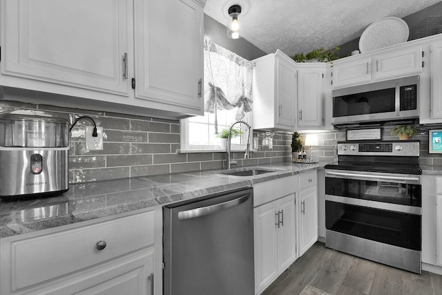 kitchen with a textured ceiling, white cabinetry, stainless steel appliances, and a sink