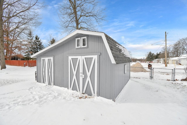 snow covered structure featuring an outbuilding and fence