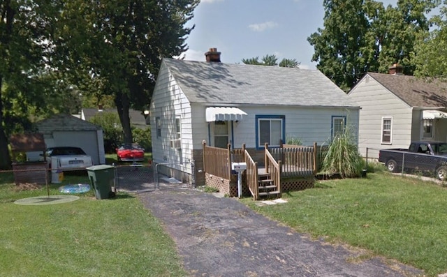 view of front of home with aphalt driveway, an outdoor structure, fence, roof with shingles, and a front lawn