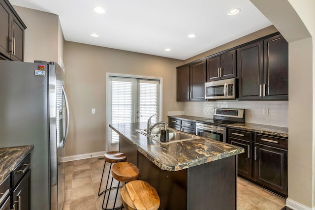 kitchen with a center island with sink, a kitchen breakfast bar, a sink, stainless steel appliances, and backsplash