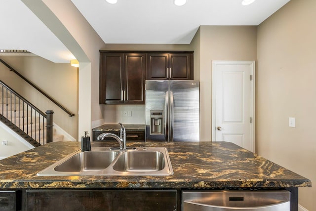 kitchen featuring arched walkways, stainless steel fridge, a sink, and dark brown cabinets