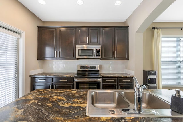 kitchen featuring appliances with stainless steel finishes, a sink, dark brown cabinetry, and decorative backsplash