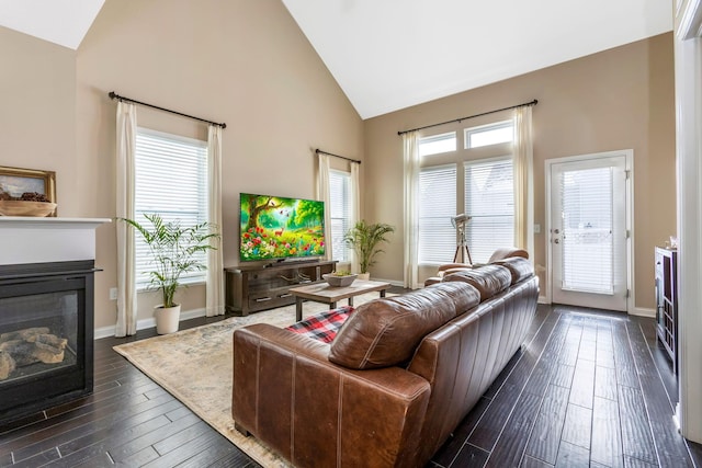 living room with high vaulted ceiling, plenty of natural light, a glass covered fireplace, and dark wood finished floors