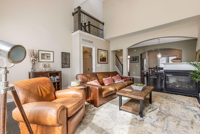 living area featuring arched walkways, visible vents, wood finished floors, baseboards, and stairs