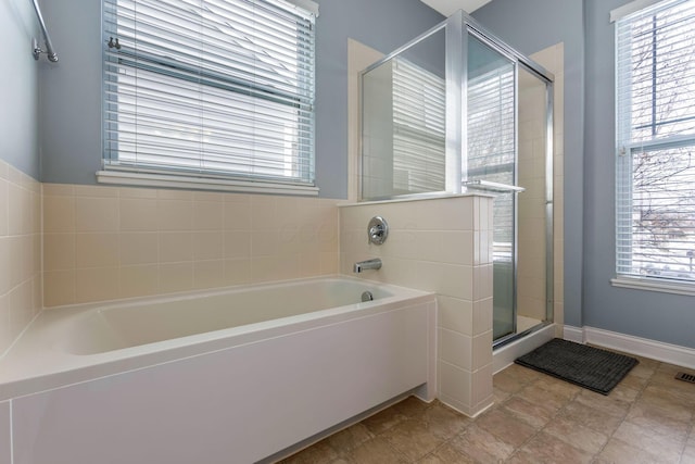 full bathroom featuring a garden tub, a shower stall, and baseboards