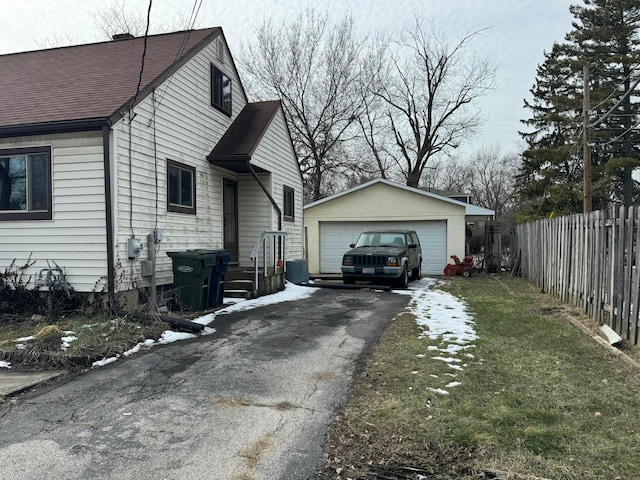 view of property exterior featuring a lawn, a detached garage, roof with shingles, an outbuilding, and fence