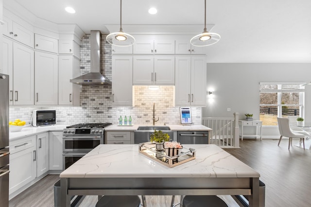 kitchen with stainless steel appliances, a sink, white cabinetry, wall chimney range hood, and pendant lighting