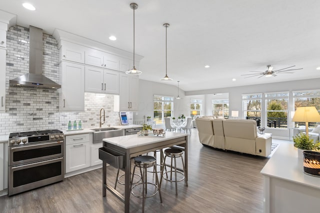 kitchen with a sink, white cabinets, light countertops, wall chimney range hood, and double oven range