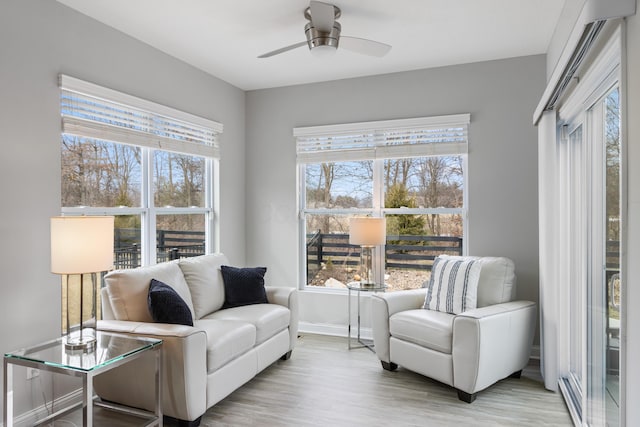 living area with light wood-type flooring, a ceiling fan, and baseboards