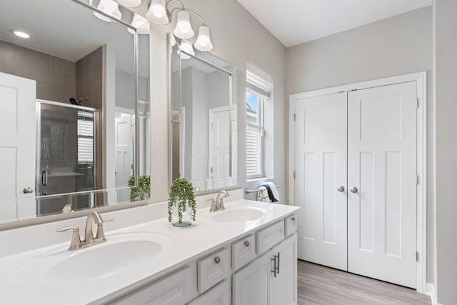 full bath featuring double vanity, wood finished floors, a sink, and a shower stall