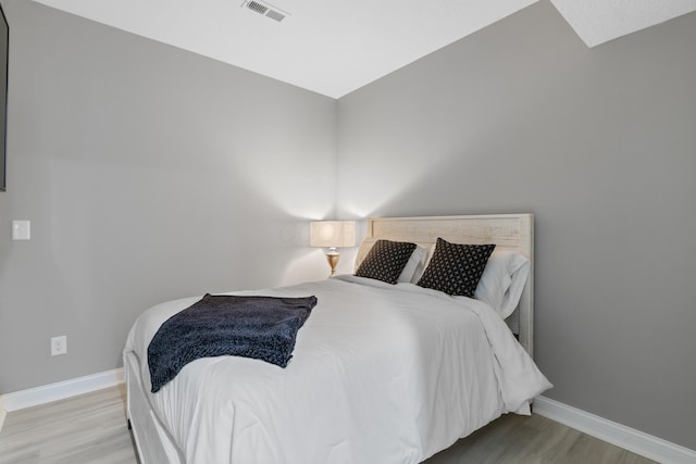 bedroom with light wood finished floors, visible vents, and baseboards