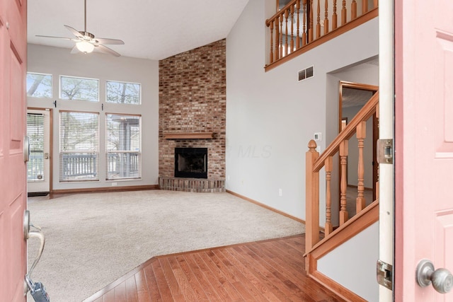 unfurnished living room with high vaulted ceiling, visible vents, ceiling fan, and stairway