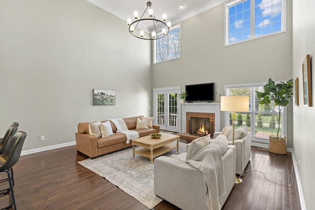 living area featuring crown molding, plenty of natural light, baseboards, a brick fireplace, and a notable chandelier