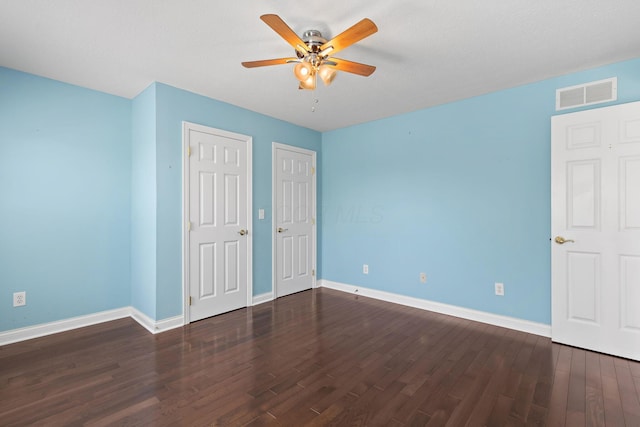 unfurnished bedroom with two closets, visible vents, baseboards, wood finished floors, and a ceiling fan