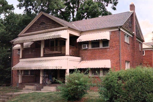 view of front of home with a balcony, covered porch, a chimney, and brick siding