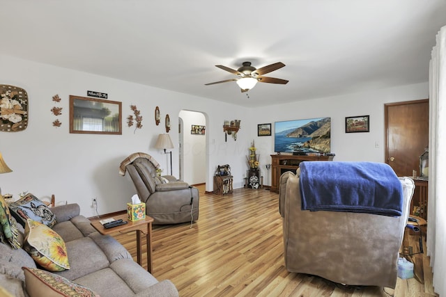 living room with arched walkways, ceiling fan, and light wood-style flooring