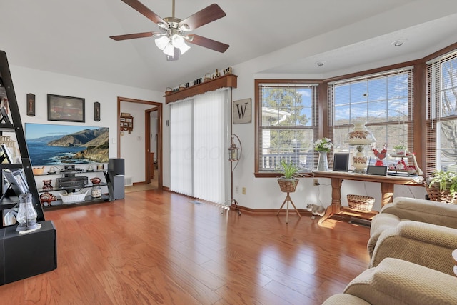 living room with ceiling fan, vaulted ceiling, baseboards, and wood finished floors