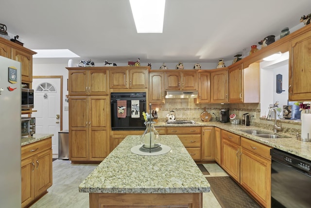 kitchen featuring light stone counters, under cabinet range hood, a sink, black appliances, and tasteful backsplash